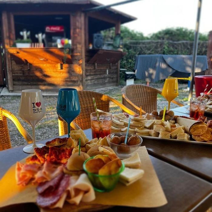Tavolo all'aperto con taglieri, patatine e calici di aperitivo davanti al chiosco in legno